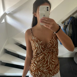 Zebramönstrad linnetopp från Garcia - Säljer en snygg zebramönstrad linnetopp från Garcia i brunt och vitt. Toppen har smala axelband, omlott-detalj framtill och en lätt croppad passform. Perfekt för dig som vill sticka ut med ett coolt mönster och somrig vibe.