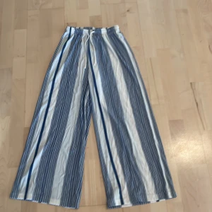 Randiga wide byxor från H&M XS - Snygga blå- och vitrandiga byxor från H&M i storlek XS. De har bred passform, resår i midjan och snörning. Materialet är en mix av viskos och polyamid, vilket gör dem lätta och luftiga. OBS! Byxorna har prislappen kvar.