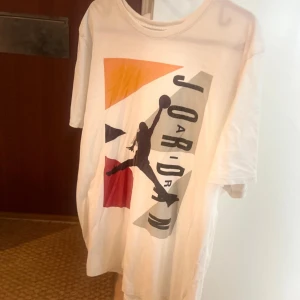 Vit Jordan t-shirt med tryck - Säljer en vit t-shirt från Jordan med stort färgglatt tryck framtill och klassisk Jumpman-logga på ryggen. T-shirten har korta ärmar och en relaxed passform. Perfekt för dig som gillar streetwear och sportig stil.