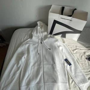 Vit hoodie från Polo Ralph Lauren - Snygg vit zip hoodie från Polo Ralph Lauren med dragkedja och klassisk logga på bröstet. Tröjan har huva med snörning, känguruficka och är tillverkad i mjuk bomull. Perfekt för en clean och stilren look. Köpte den från Nk i Göteborg för ca 3 månader sen. Alla prislappar och sånt är kvar. Aldrig använd bara testad en gång. Kom privat för mer info/bilder.😁
