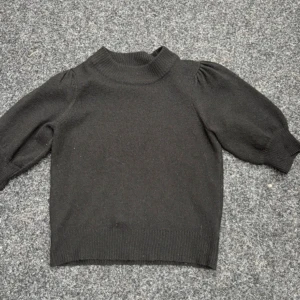 Svart stickad tröja med puffärm - Svart stickad tröja med puffiga trekvartsärmar och ribbad halsringning. Enkel och stilren design som passar till jeans eller kjol. Mjuk och skön känsla tack vare det stickade materialet. Perfekt för dig som gillar minimalistisk stil.