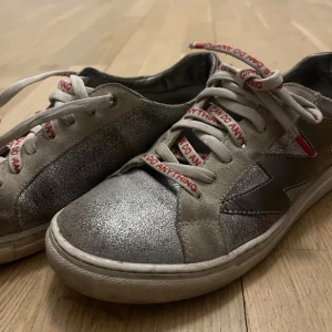 Silvriga glittriga sneakers med text från Zadig  - Snygga sneakers i silver med glittriga detaljer och grå mocka. Skorna har vita snören med röd text 'I CAN DO ANYTHING' och en vit sula. Perfekta för dig som vill sticka ut med en cool och unik stil.