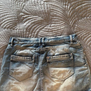 Blå jeanskjol med fickor - Säljer en klassisk blå jeanskjol i kort modell med fem fickor, bälteshällor och knappstängning fram. Kjolen har en rak passform och är tillverkad i denim med snygg tvättad look. Perfekt för dig som gillar en avslappnad och cool stil.