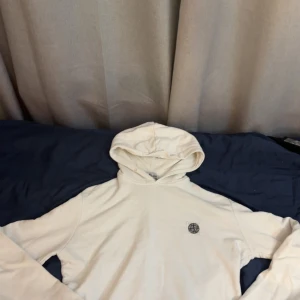 Vit hoodie från Stone Island - Säljer en stilren vit hoodie från Stone Island med klassisk logga på bröstet. Tröjan har huva och långa ärmar, perfekt för en clean och avslappnad look. Passar dig som gillar streetwear och enkel design.