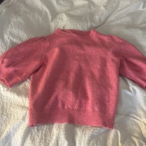 Rosa stickad tröja från Vero Moda - Superfin rosa stickad tröja från Vero Moda med korta puffärmar och ribbade muddar. Tröjan har en rund halsringning och är i en mjuk, mysig kvalitet som passar perfekt till både jeans och kjol. Enkel men ändå söt med sin puffiga ärm.