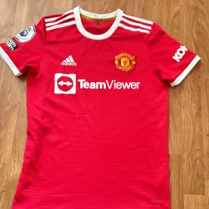 Manchester United Adidas matchtröja S - Röd Manchester United fotbollströja från Adidas med vita detaljer och klubbmärke på bröstet. Premier League-märke på ärmen, TeamViewer-tryck på framsidan och klassiska Adidas-ränder på axlarna. 200kr är sista pris .