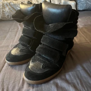 !!!INTRESSEKOLL!!! Svarta sneakers Isabel Marant strl 38 - (LÅNADE BILDER!!) Coola svarta sneakers från Isabel Marant med chunky design och breda kardborreband. Skorna har en mix av mocka och skinn, rund tå och beige sula. Perfekta för dig som vill ha en statement-sneaker med streetkänsla. 