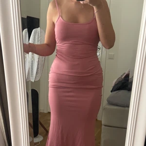 Rosa långklänning med smala axelband - Säljer en snygg rosa långklänning med smala axelband och figurnära passform. Klänningen är ärmlös och har en enkel, stilren design som framhäver siluetten. Perfekt för dig som gillar en feminin och modern look. Lappen är tyvärr inte kvar men jag har köpt den på en marknad i Spanien och skulle gissa på att den är i storlek S men är ganska stretchig.