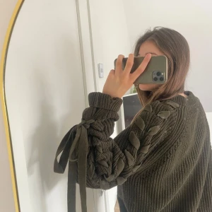 Olivgrön stickad tröja med snörning - Säljer en olivgrön ribbad tröja med snörningsdetaljer längs armarna. Tröjan har två hål för tummarna🥰🥰