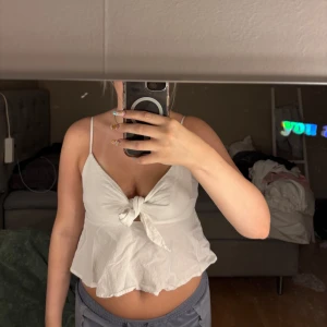 Vit linnetopp med knyt framtill - Supersöt vit linnetopp med smala axelband och knyt framtill. Toppen har en lätt volangig nederkant och är perfekt för varma dagar. Sitter löst och har en feminin v-ringning. Enkel att matcha med jeans eller kjol.