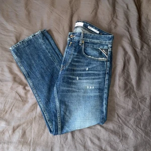 Replay Grover med slitningar - Snygga Replay Grover jeans i klassisk blå tvätt med slitningar och raka ben. Jeansen har fem fickor, tydliga kontrastsömmar och Replay-logga på fickan. Modellen är straight fit och passar dig som gillar en tidlös look med lite edge.