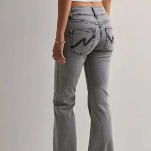 Grå bootcut jeans med broderade fickor - Snygga grå jeans med bootcut passform och coola svarta broderier på bakfickorna. Jeansen har klassisk femficksdesign. Dom har gått sönder lite och blivit missfärgad då dom varit för långa för mig! (Bild 3 och 4)