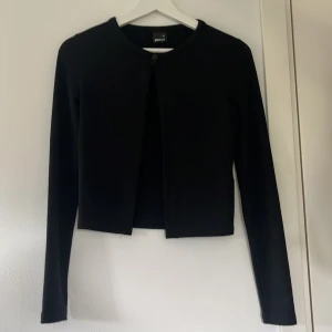 Svart kofta från Gina Tricot XS - En svart kofta från Gina Tricot i storlek XS. Koftan har rund halsringning, lång ärm och stängs med en knapp upptill. 
