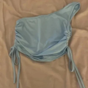 Ljusblå oneshoulder topp från SHEIN - Supersnygg ljusblå oneshoulder topp från SHEIN med cool snörning på båda sidorna. Gjord i mjuk polyester som sitter skönt mot huden. Perfekt för dig som gillar trendiga detaljer och vill sticka ut med en unik form.