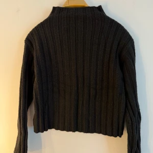 Ribbstickad tröja - Svart, ribbstickad tröja med hög krage och långa ärmar. Tröjan är kort i modellen. Smått nopprig, se bild 2. Storlek S