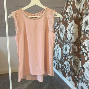 Ljusrosa blus med pärldetaljer - Supersöt ljusrosa blus med ärmlös design och spetsdetaljer på axlarna. Rund halsringning med pärlor🩷Är inte helt säker på storleken men det borde vara xs eller s. 