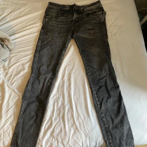 Replay Anbass slim fit jeans svart - Snygga Replay Anbass slim fit jeans i svart tvättad denim med slitningar och klassiska fem fickor. Byxorna har dragkedja, smal passform och detaljerade sömmar på bakfickorna. Perfekt för dig som gillar en modern och stilren look. Hör av er för mer info!