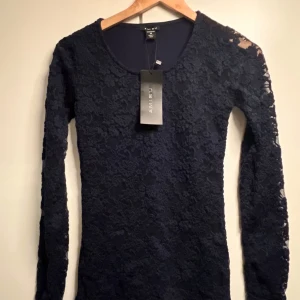 Marinblå spetsklänning från Amisu XS - Snygg marinblå kortklänning från Amisu i storlek XS. Klänningen har långärmade spetsärmar och ett blommigt spetsmönster över hela framsidan. Rund halsringning och figurnära passform ger en elegant look. Perfekt för dig som gillar stilrena detaljer och mörka färger.