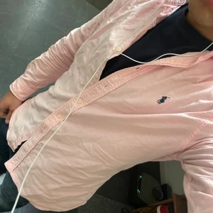 Rosa skjorta från Ralph Lauren - Ljusrosa skjorta från Ralph Lauren med klassisk krage och långärmad design. Storleken är S, men skulle säga att den är nånstans mellan S och M. Väldigt bra skick då den är sparsamt använd!