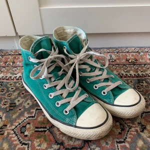 Turkosa Converse All Star high tops - Säljer ett par klassiska Converse All Star high tops i en snygg turkosgrön färg. De är stora i storlekan så skulle säga att de är mer strl 39. Skorna har vit gummisula, rund tå och vita snören. Märkets ikoniska logga på sidan och bak. Tillverkade i slitstark bomullstextil, perfekt för dig som gillar retrostil.