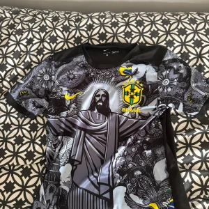 Nike Brasil CBF Dri-Fit fotbollströja M - Unik Brasil CBF fotbollströja från Nike med Dri-Fit material. Tröjan har ett detaljerat grafiskt tryck med Kristusstatyn, brasilianska flaggan och CBF-emblem i gult och grönt. Svart bas med inslag av grått och vitt, korta ärmar och rund hals. Perfekt för dig som gillar snygga och originella matchtröjor. Pris går att diskutera!