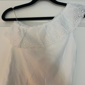 Vit offshoulder klänning Kappahl - Supersöt vit offshoulder blus från Kappahl med bred volang upptill och broderade spetsdetaljer. Perfekt för sommarens alla tillfällen, med en luftig och lätt känsla. Blusen har en feminin och fräsch look som är enkel att styla.