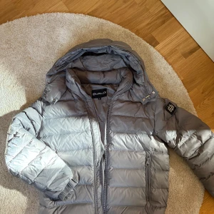 Grå pufferjacka från Bvaldi med huva - Säljer en grå pufferjacka från Bvaldi med stor huva och dragkedja framtill. Jackan har quiltad design, två fickor med dragkedja och en patch på ärmen. Perfekt för kalla dagar och riktigt snygg till alla sorts stilar. Köpt för 2999kr på bvaldis egna hemsida. Skicket är 9,5 av 10 använd max 3 gånger då jag beställde en storlek för liten och den blev för liten direkt. Kom gärna med bud eller frågor, byten kan godkännas, helst byte mot andra jackor eller västar som colmar, moncler men annat oxå ✅💯😁