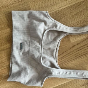 Beige ribbad linnetopp Aim'n XS - Säljer en beige ribbad linnetopp från Aim'n i storlek XS. Toppen har breda axelband och en croppad passform, perfekt för träning eller chill. Tillverkad i mjuk och stretchig polyesterblandning som sitter skönt mot kroppen.