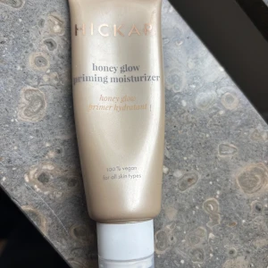 Hickap Honey Glow Priming Moisturizer - Säljer en lyxig Honey Glow Priming Moisturizer från Hickap. Tuben är skimrande guldbeige med vit kork och innehåller en vegansk primer som ger glow och återfuktning. Passar alla hudtyper och är perfekt som bas innan smink. Smidig tub med modern design.