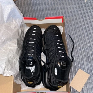 Nike Air Max Plus Tn Svarta sneakers - Nike Air Max Plus Tn sneakers i helsvart med vita detaljer på snörningen. Skorna har mesh och syntet på ovandelen, synlig Air Max-dämpning i sulan och Tn Air-logga bak. Snygg, sportig vibe och riktigt bekväma för dig som gillar streetstyle.