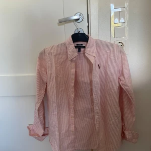 Rosa och vit randig skjorta Ralph Lauren - Snygg slim fit skjorta från Ralph Lauren i rosa och vitt med smala ränder. Klassisk krage, långärmad och med knappar hela vägen framtill. Ikoniska broderade loggan på bröstet. Perfekt för dig som gillar stilrena och fräscha plagg. Pris kan diskuteras vid snabb och smidig affär! 