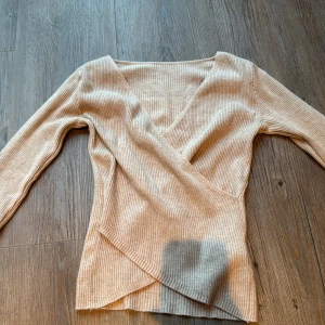 Beige omlottop från SHEIN - Snygg beige omlottop från SHEIN i ribbad, mjuk polyesterblandning. Toppen har lång ärm, v-ringad hals och omlottdetalj framtill som ger en cool och trendig look. Perfekt att styla med jeans eller kjol för en chill vibe.