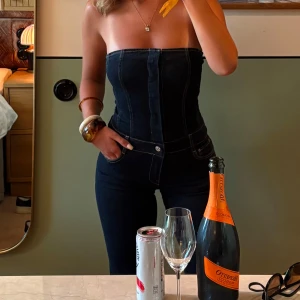 Mörkblå bandeau - jeansbyxdress - Säljer en snygg mörkblå jeansbyxdress med markerad söm och knappar framtills. Byxdressen har hög midja, bandeau och långa-ben, vilket gör att den passar alla längder (jag är 175). Materialet är klassiskt jeans med kontrastsömmar och fickor på sidorna. Man knäpper med ett blixtlås nertill och sedan knappar upptill, någon knapp har gått av men det påverkar ingenting. Skriv för fler bilder eller frågor🩷