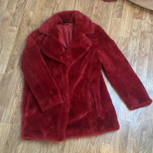 Röd pälsjacka från HM - Röd jacka i fuskpäls från HM Divided i storlek S. Jackan har fluffigt fuskpälsmaterial, bred krage och dolda tryckknappar framtill. Använd fåtal gånger.