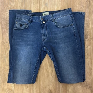 Blå Steve Satin Jeans från Morris - Snygga blå jeans från Morris, modell Steve Satin Jeans. Klassisk femficksdesign med coola detaljer som broderad logga på myntfickan och specialdesignade knappar. Jeansen har en rak passform och är tillverkade i mjukt jeanstyg med lätt tvättad look.