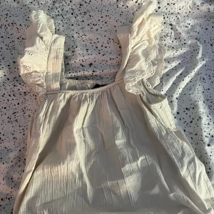 Sommartopp  - Supersöt sommartopp från Vero Moda i storlek XS. Toppen har breda axelband med romantiska volanger och broderade detaljer. Tillverkad i mjuk bomull med lätt struktur, perfekt för sommarens alla tillfällen. Säljes då den inte kommer till användning längre.