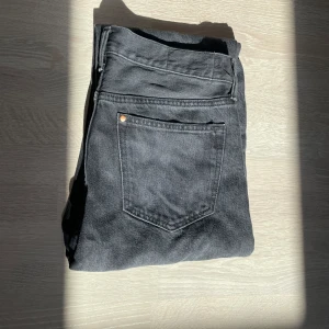 Svarta jeansbyxor med straight fit - Säljer ett par svarta jeansbyxor med klassisk femficksdesign och raka ben. Jeansen har silverfärgade nitar och knapp, samt bälteshällor. Materialet är slitstarkt jeans och färgen är mörk.