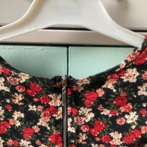 🍒Blommig croppad topp🍒 - 🍒SUNFLOWER🍒Supersöt långärmad topp med blommigt mönster i rött, beige och grönt på svart botten. Croppad modell med rund hals och dragkedja i ryggen. Kommer i ett mjukt material med bomull och lite stretch.🍒