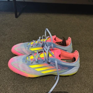 Adidas färgglada fotbollsskor - Säljer ett par Adidas fotbollsskor med en riktigt cool färgkombo i ljusblått, rosa och neon-gult. Skorna har snörning, spetsig tå och mönstrad sula med dobbar för grymt grepp på planen. Ovandelen är i syntetmaterial och insidan är mjukt fodrad för extra komfort. Använda 1 gång. Nypris ligger på 1600