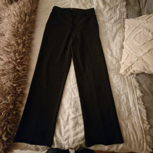 Svarta wide kostymbyxor Gina Tricot - Snygga svarta kostymbyxor från Gina Tricot i storlek 34. Byxorna har en klassisk wide passform med raka ben, bälteshällor och diskreta bakfickor. Perfekta för en clean och stilren look. Materialet är mjukt och har en lätt stretch för extra komfort. Finns en vit fläck på baksidan (som man kan se på sista bilden) annars är det inget bra skick!
