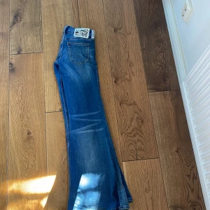 Blå bootcut jeans från Cheap Monday - Säljer ett par blå jeans från Cheap Monday med låg midja och bootcut passform. Jeansen har klassiska fem fickor, slitningar och snygg tvättad look. Materialet är mjukt denim som sitter skönt och ger en cool vibe. Lite små i storlek, skulle säga att dem är som storlek 25