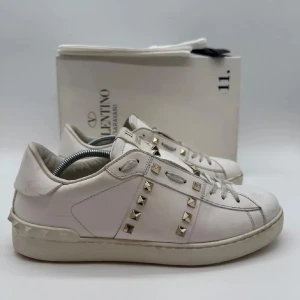 Valentino Rockstud vita sneakers - Snygga vita Valentino Garavani Rockstud sneakers med ikoniska guldfärgade nitar längs sidorna och på tungan. I jättebra skick, medföljer INTE box utan Extra nitar samt extra skosnöre. Köpta på Deluxswe, därav äkta! Storlek 41❤️