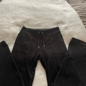 Svarta Juicy Couture byxor  - Svarta byxor från Juicy Couture i storlek S. Byxorna har bred resår i midjan med snörning, stora fickor fram och bak med knappdetaljer. Mjukt och skönt material som ger en chill vibe, perfekt för att hänga hemma eller dra ut med kompisar.