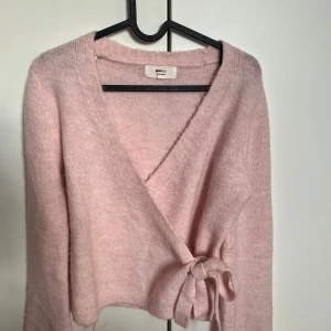 Ljusrosa stickad kofta från Gina Tricot - Supermysig ljusrosa omlottkofta från Gina Tricot. Koftan har v-ringad hals, långa ärmar och knyt i sidan för en snygg passform. Perfekt att slänga på sig när det är lite kyligt ute. Passar dig som gillar en chill och feminin stil. Ett snöre på koftan är lite sönder men det är inget man ser. Använd Max 5 gånger💗