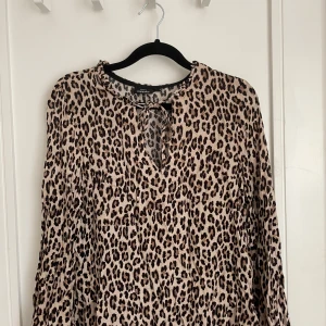 Leopardmönstrad blus från Kappahl - Säljer en snygg leopardmönstrad blus från Kappahl med beige och svarta toner. Blusen har långa ärmar, rund hals med liten volangkant och knytning fram. Materialet är mjukt och lätt.