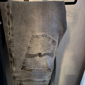 Grå Nudie Jeans Grim Tim 30/30 - Snygga grå jeans från Nudie Jeans, modellen Grim Tim Dark Cove. De har klassisk femficksdesign med coola sömmar på bakfickan och detaljer i kopparfärgad metall. De är köpta nya hos nudie i stockholm. Jättefint skick då de är sparsamt använda. Om de är några frågor är de bara o höra av sig!