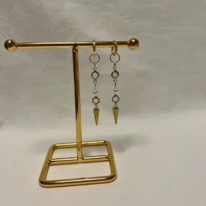 Guldiga örhängen med pärlor och spikes - Unika örhängen i guld med hängande detaljer, små vita pärlor och glittriga ringar. Spetsiga spikes ger en edgy vibe och de glittriga detaljerna gör dem extra snygga. Perfekta för dig som vill sticka ut med coola accessoarer.