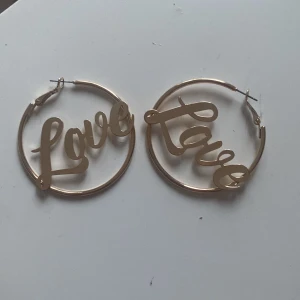 Guldiga hoop-örhängen med text - Säljer ett par stora hoop-örhängen i guld med cool textdesign där det står 'Love' i varje ring. 
