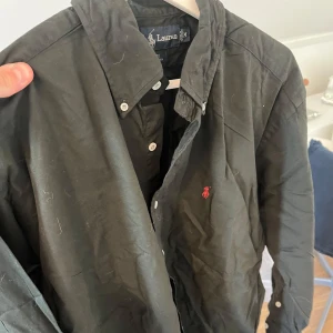 Svart Ralph lauren skjorta - Svart Ralph lauren skjorta i storlek M, bra skick utan fläckar! Stor på mig som är 184cm och 70kg Pris kan diskuteras