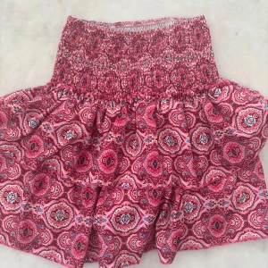 Rosa kortkjol med mönster - Säljer en söt rosa kortkjol med elastisk midja och färgglatt paisley-inspirerat mönster i rött, blått och vitt. Kjolen har en volangig form och är gjord i mjukt bomullstyg som är skönt mot huden. Perfekt för dig som gillar färg och mönster!